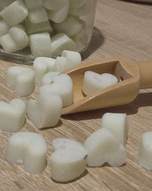 Heart-shaped wax melts in a glass jar with a wooden scoop on a wooden surface.
