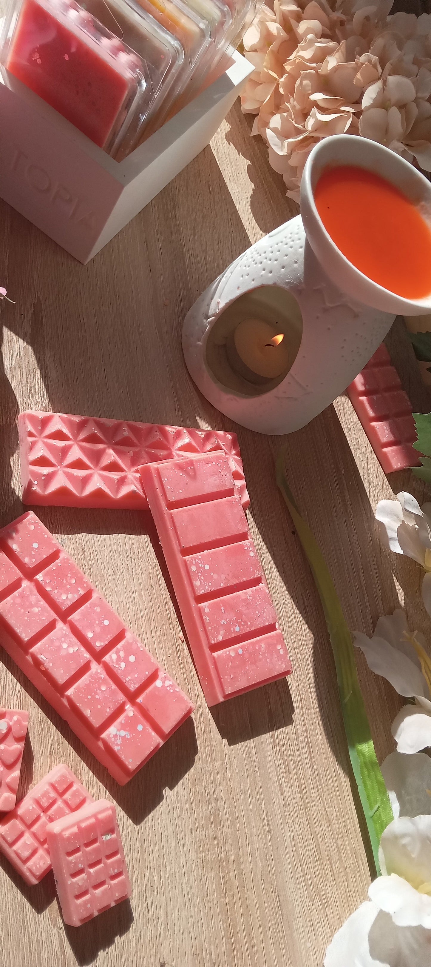 Pink wax melts on a wooden surface with a lit candle and decorative elements.