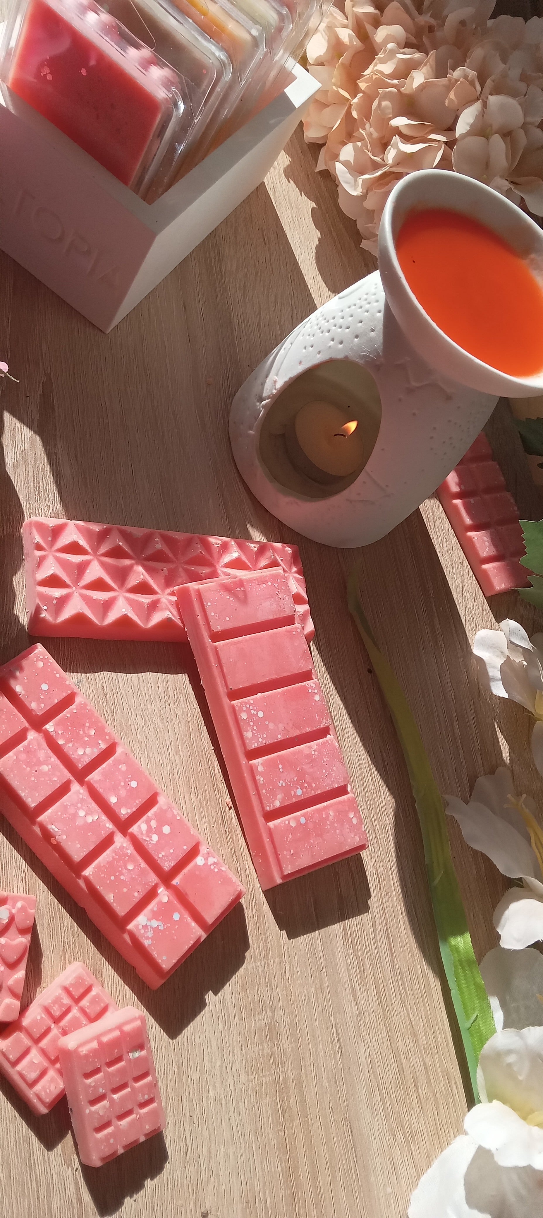 Pink wax melts on a wooden surface with a lit candle and decorative elements.