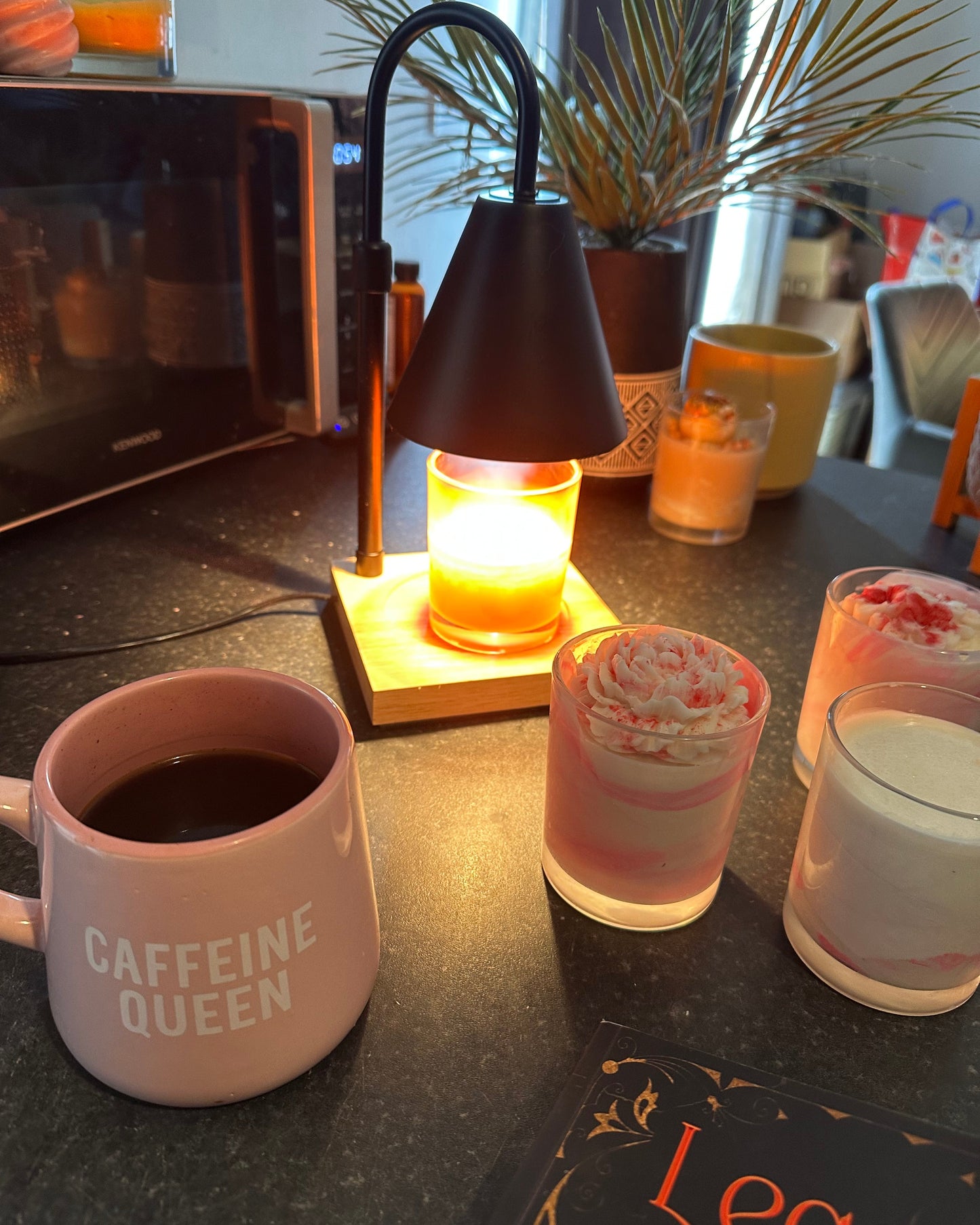 Pink mug labeled 'Caffeine Queen' on a table with a lit candle and plants.
