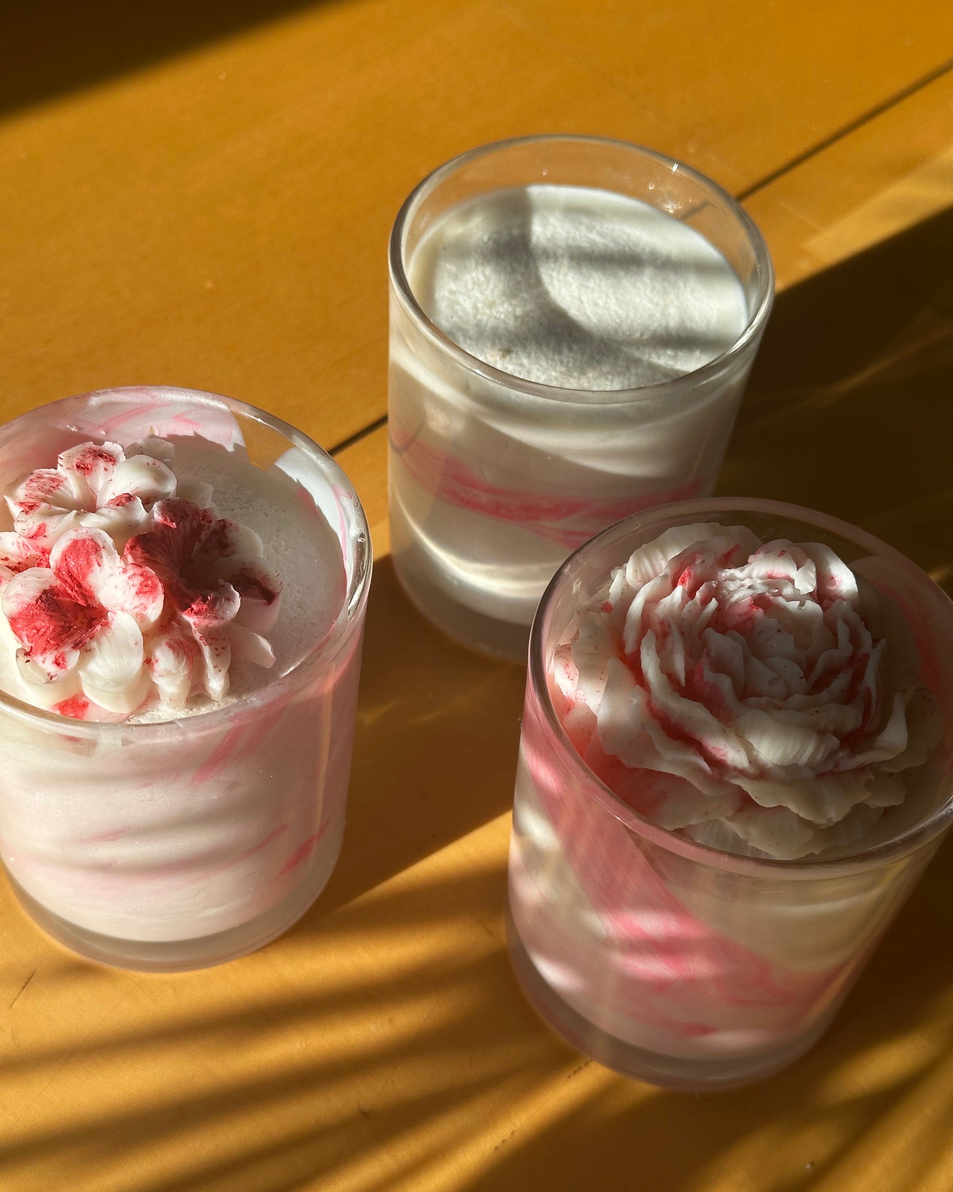 three pink and white Yuzu & Dragonfruit scented coconut wax wickless candles with pink and white coconut wax melts on the top in clear glass candle jars on a wooden surface.
